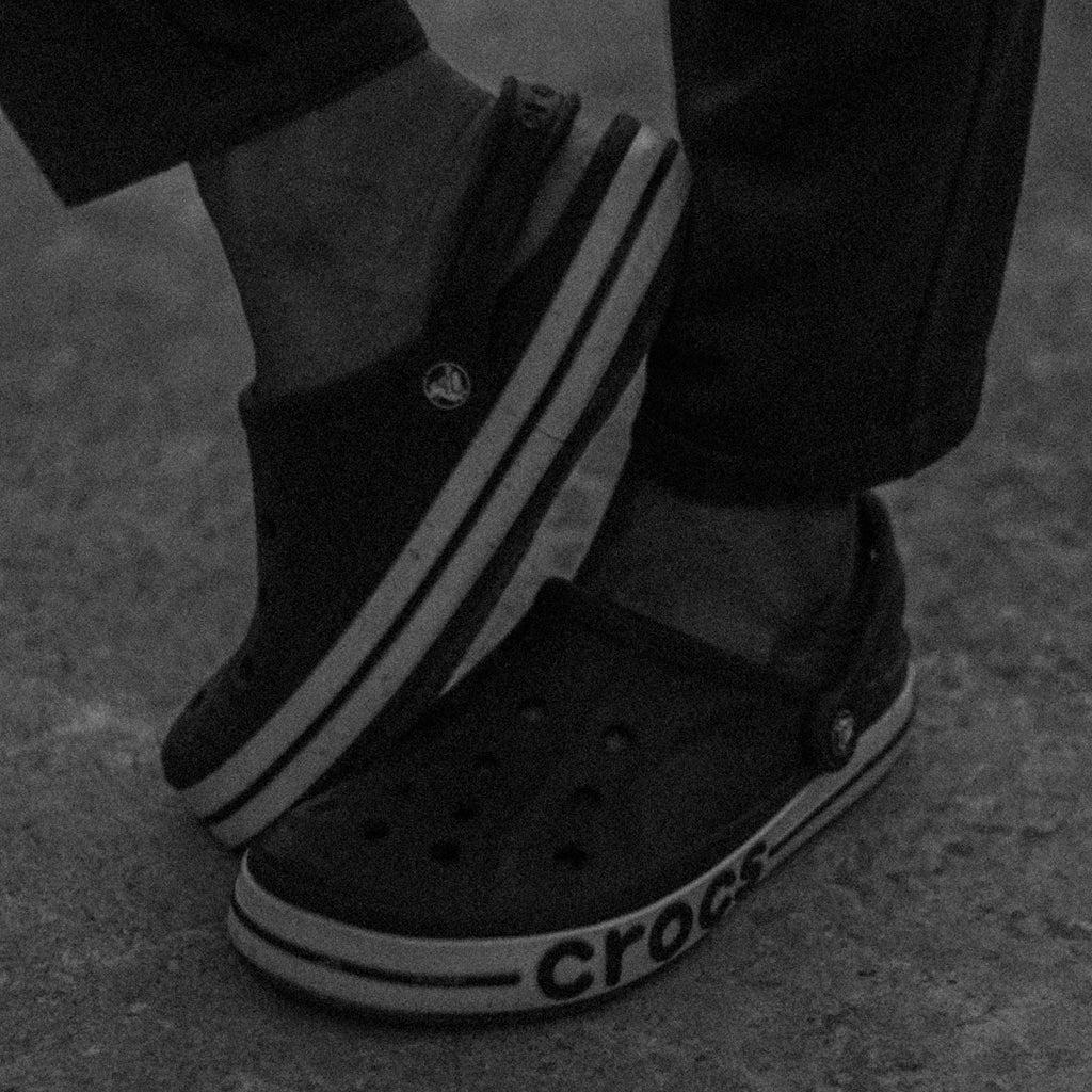 Close up of a person wearing black Crocs with striped soles standing on a concrete surface in a casual setting