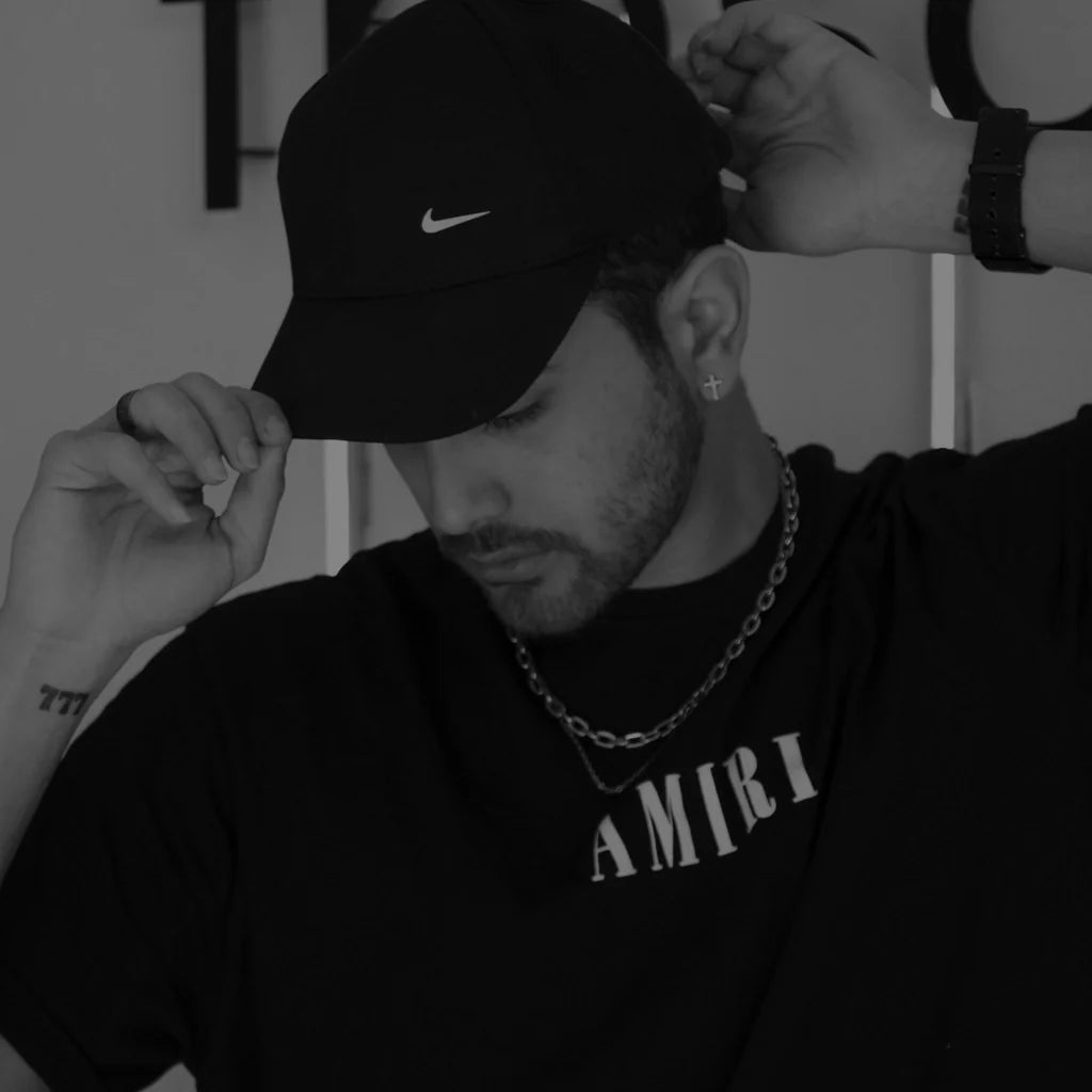 Man wearing an Amiri t-shirt, Nike cap, and silver chain, embodying luxury fashion with an effortless streetwear edge. The black-and-white style highlights the blend of high-end and affordable fashion, perfect for trendsetters in Essex.