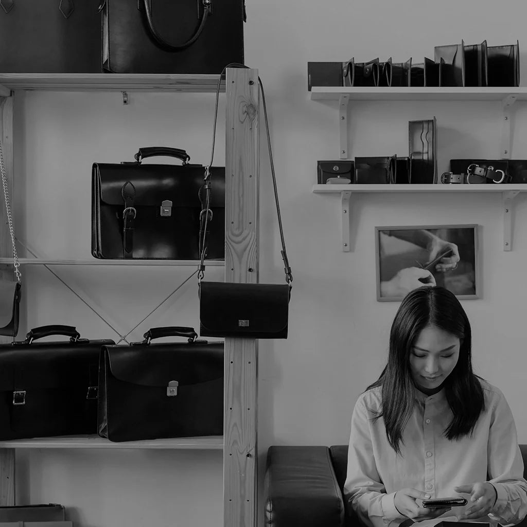 Woman sitting next to designer handbags from the EDRM Women’s Bags collection, showcasing women’s luxury fashion UK and authentic designer clothes UK available at your online luxury fashion store