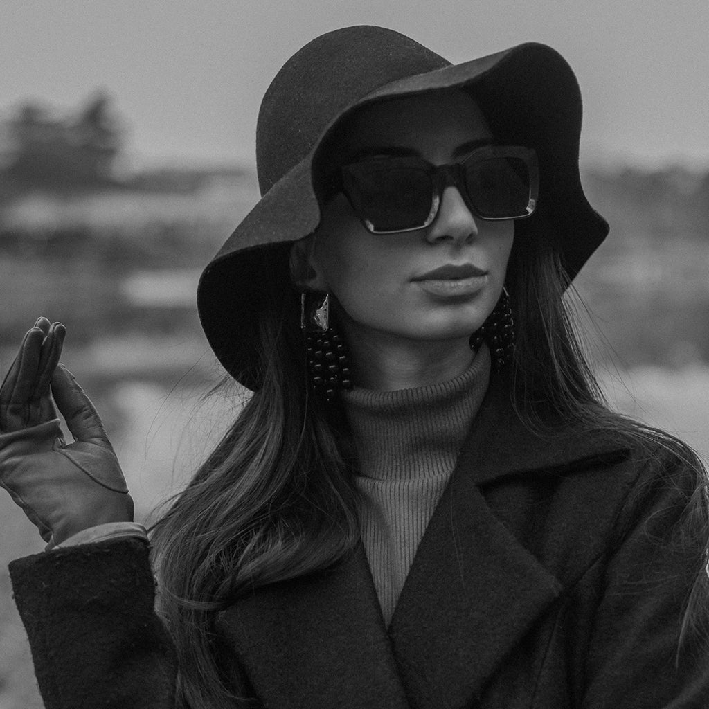 Woman in black coat, black sunglasses, and black hat, exemplifying chic street style.